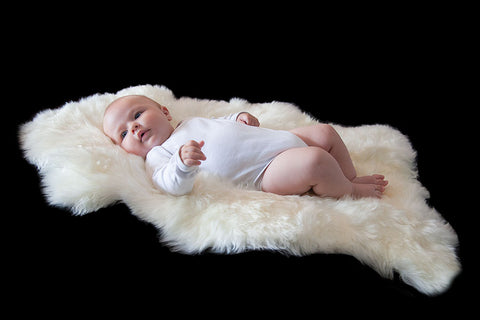 Baby happily lying on a white long wool sheepskin rug..