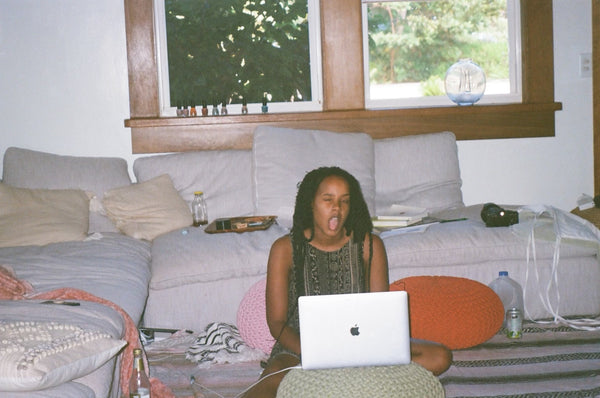 scottie. seated on the floor, in front of a couch, with her laptop in front of her.