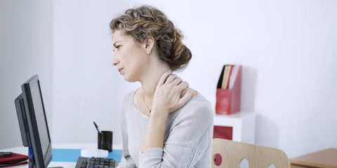 Femme avec des douleurs cervicales au travail sur ordinateur.