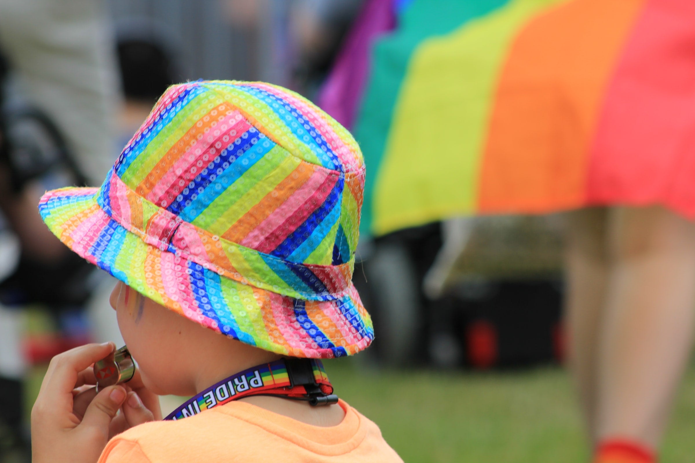 child in rainbow bucket hat and rainbow pride lanyard at family friendly pride