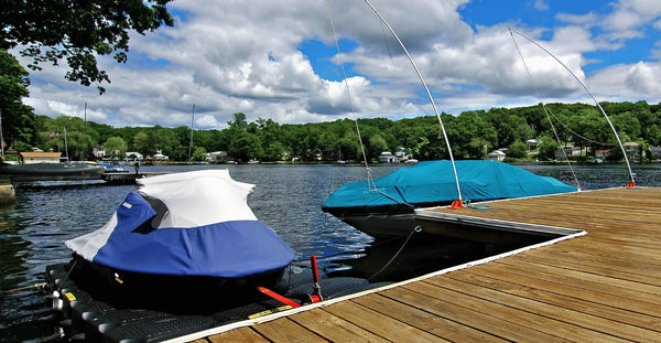 Speed boat and jet ski tied up on a lake dock on a sunny day.