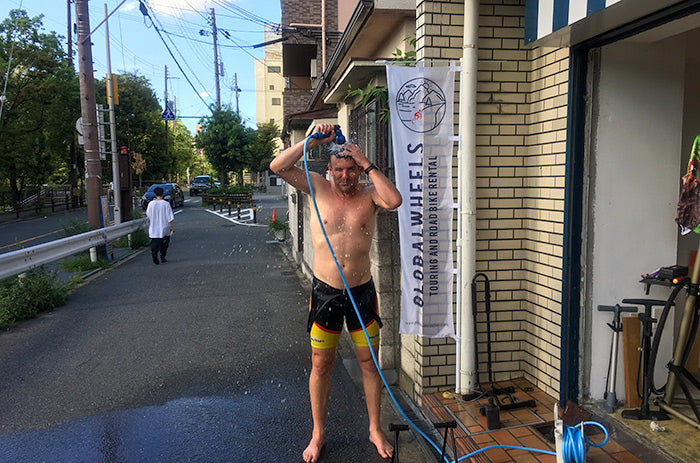 A cyclist cooling down with water from the hose outside Globalwheels' shop in Osaka.