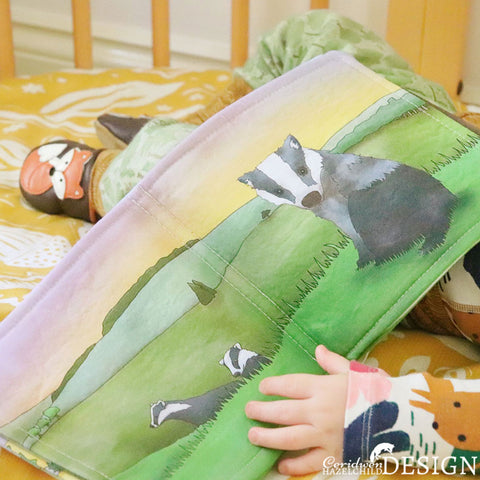 A baby holding a handmade fabric book featuring a badger illustration.
