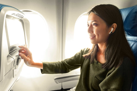 asian lady on a plane wearing airpods and tapping on the touchscreen tv whilst the twelve south airfly bluetooth transmitted is plugged into the headphone socket