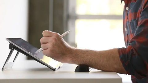 man rests his wrist on a wrist rest whilst holding an apple pencil and working on his iPad. the iPad is laid on an elevation lab drafttable stand.