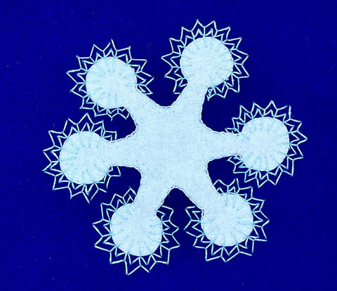 A white wool appliqué snowflake on a blue wool background embellished with fly stitches.