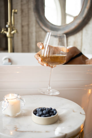 a woman relaxing in a bathtub with a glass of wine, blueberries and a candle