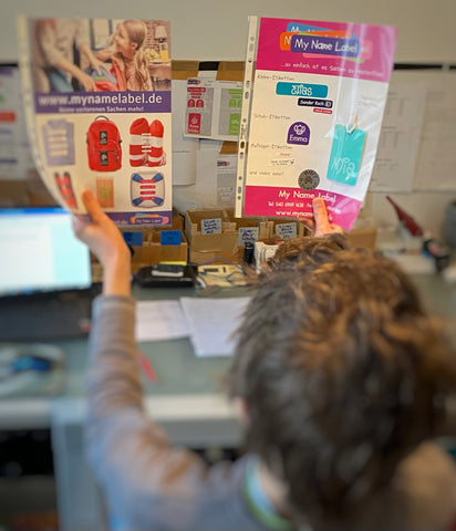 Kopf eines Jungen, der zwei Poster mit My Name Label-Produkten hochhält