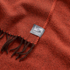 A close up image of a merino wool throw with a pattern of brown and red diagonal stripes.
