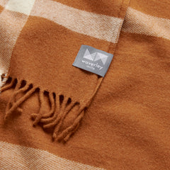 A close up image of a merino wool throw in tan with a pale cream plaid pattern.