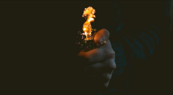 A lighter being lit in the dark with flames. 