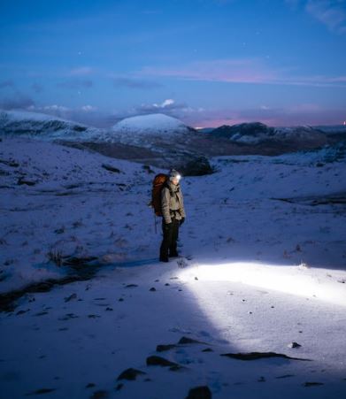 Hiker wearing a head lamp looking around at a twilight arctic landscape. 