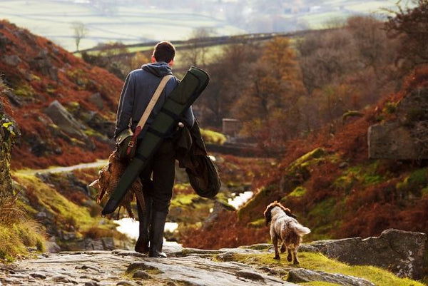 Man walking dog through wilderness going on a hunt.