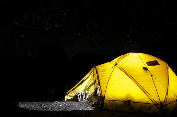 A lit tent at night with hiking shoes set outside the entrance.