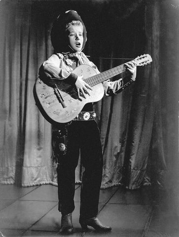 Johnny Hallyday jouant de la guitare habillé en cow-boy en 1956