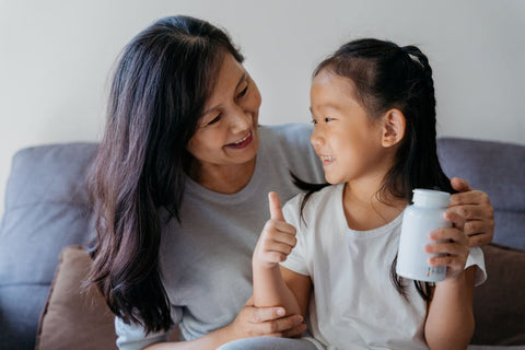 girl holding vegan vitamin bottle laughing with mom