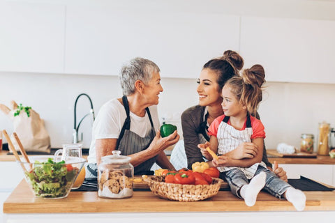 girl with mom and grandma in kitchen with vegetables and salad on table