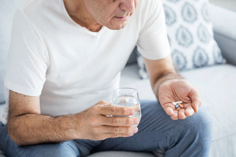man over 40 sitting on couch holding vitamins in hand