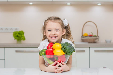 Little cute preschool girl in the kitchen with bowl of vegetables