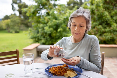 old woman taking vitamins with breakfast