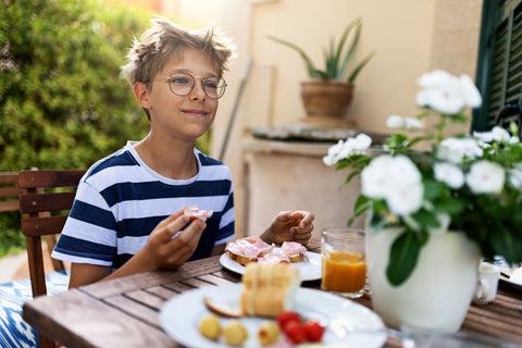 teen boy eating breakfast vegetables at table in backyard