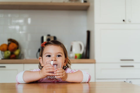 Toddler girl drinks juice from glass at home in kitchen