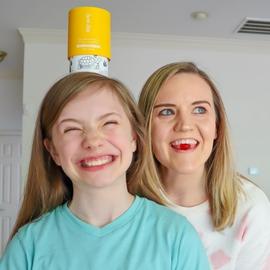 a mom and daughter playing, with a vitamin bottle on the kids head