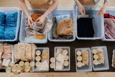 Two persons packing clothes and cans into boxes. 