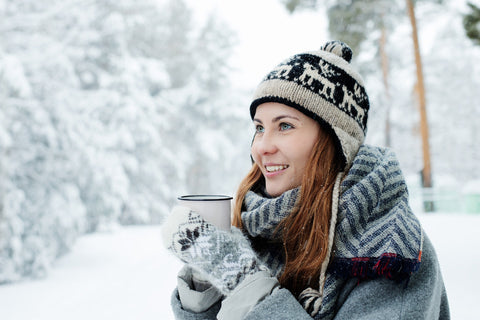 A girl in winter hat drinking tea outside in the snow.