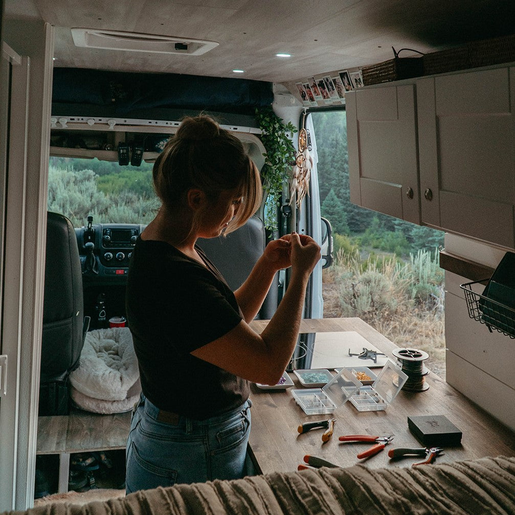 the owner of Topaz & Pearl making handcrafted jewelry inside her campervan jewelry studio