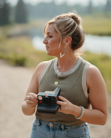 woman holding polaroid camera taking photos wearing jewelry