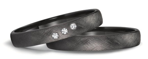 picture of a black wedding ring set, in black zirconium for men and woman. Brushed finish on the rings. One ring is set with three small diamonds