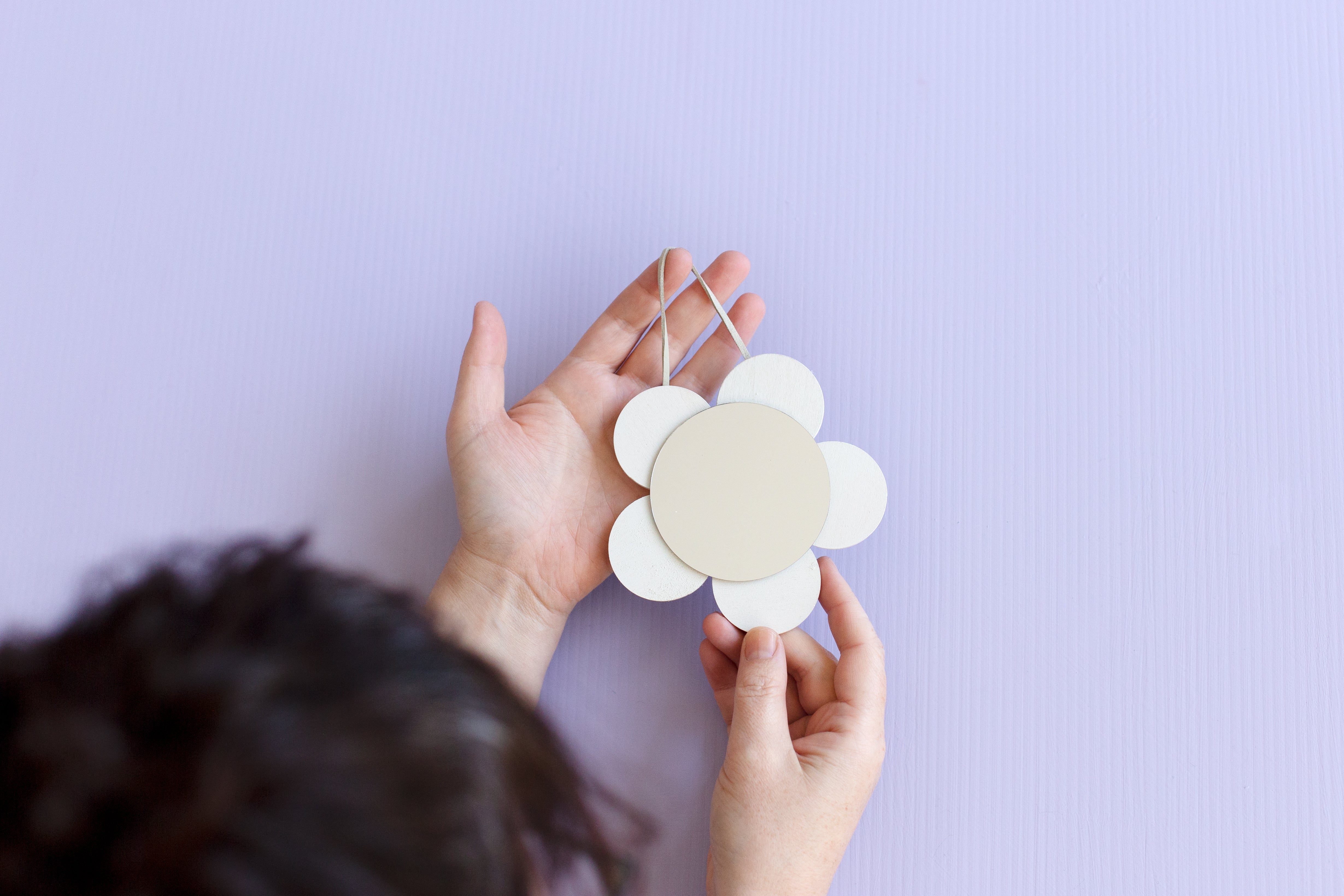 A hand holds the completed flower shaped mirror on a lilac background.