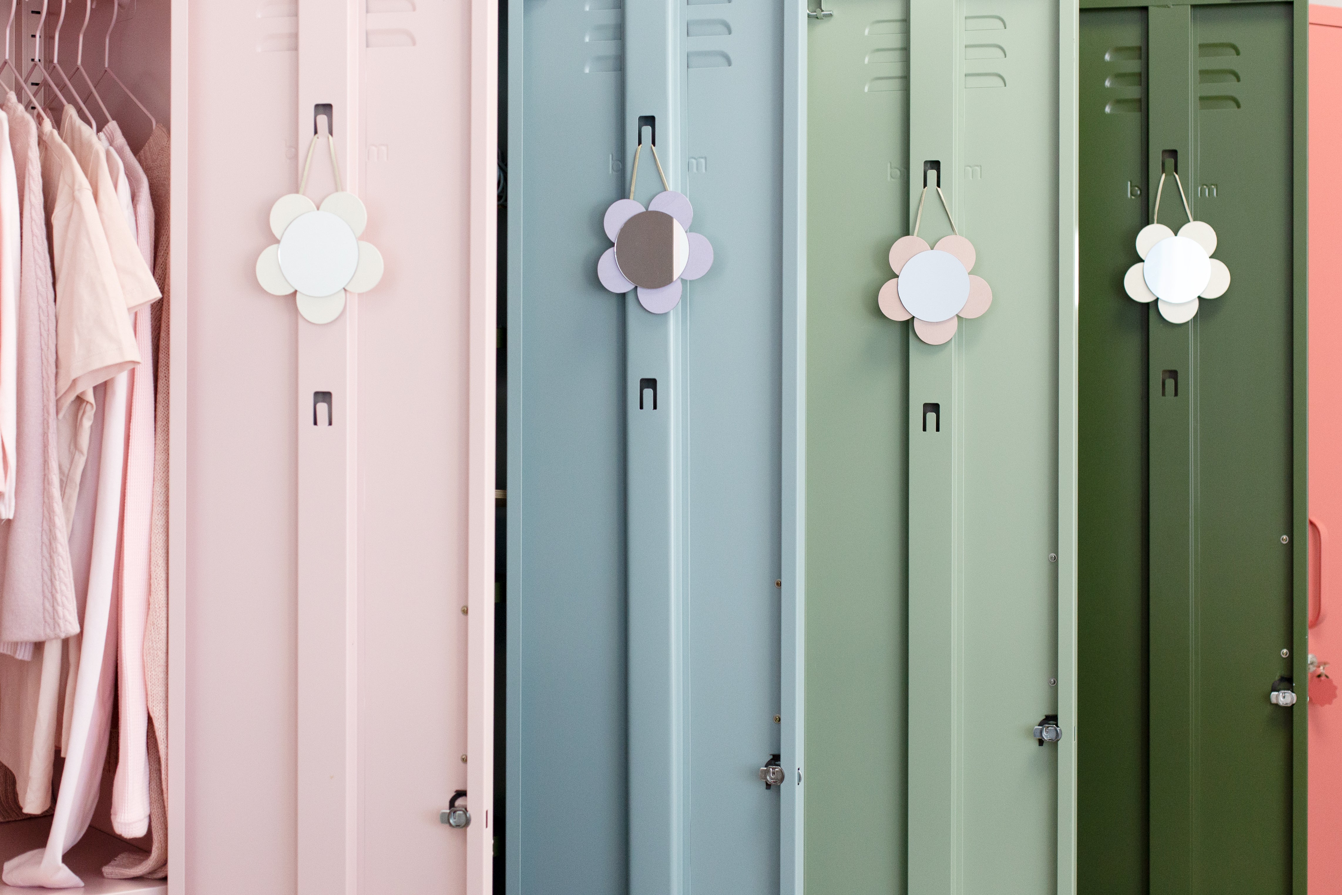 A line of four lockers, all with their doors open. A pale blush pink locker, a darker pink Berry locker, a pale Sage green locker and a darker Olive green locker. They all have flower mirrors hanging on the inside of their doors. 