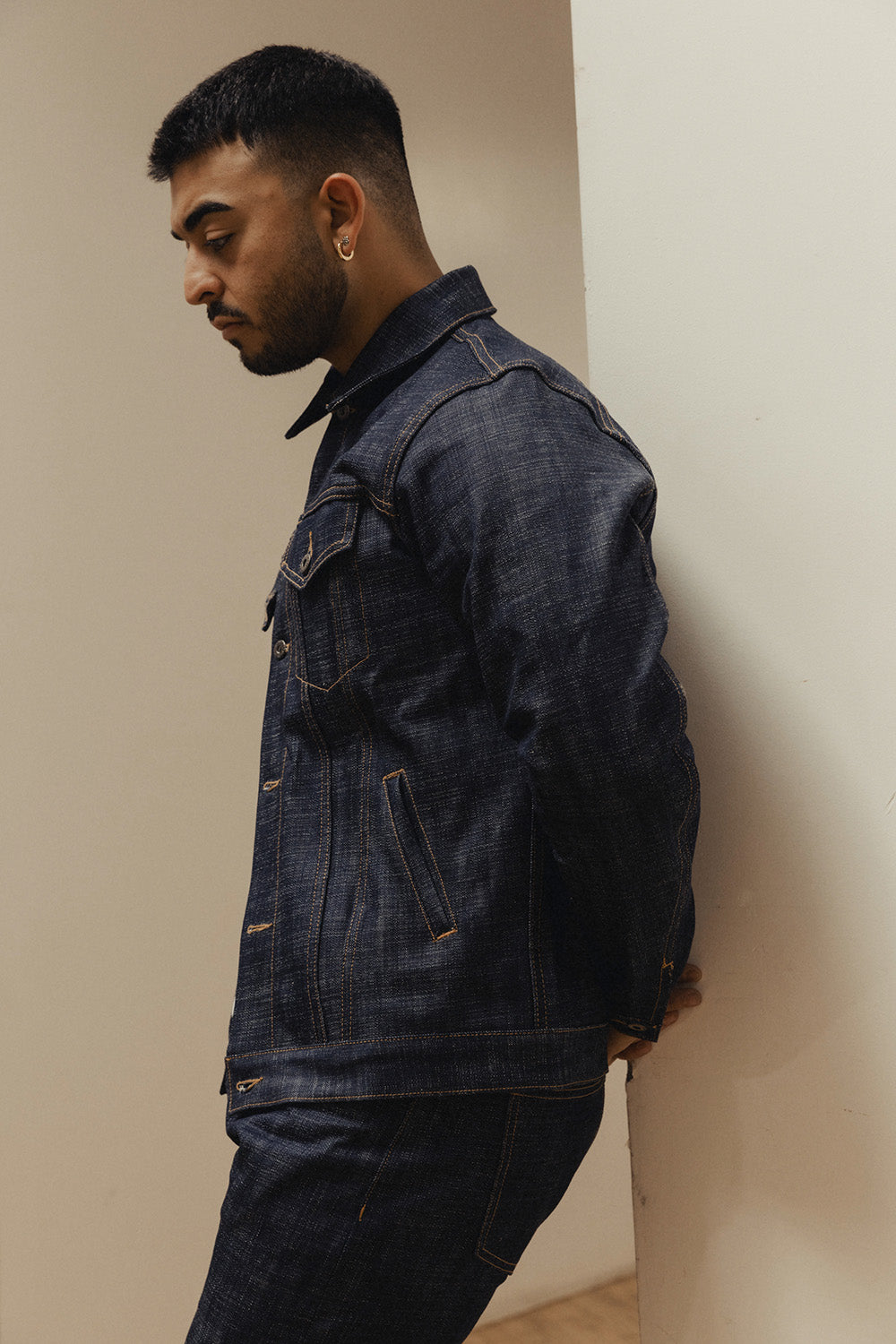 A side profile image of a man in a dark blue denim jacket and jeans.