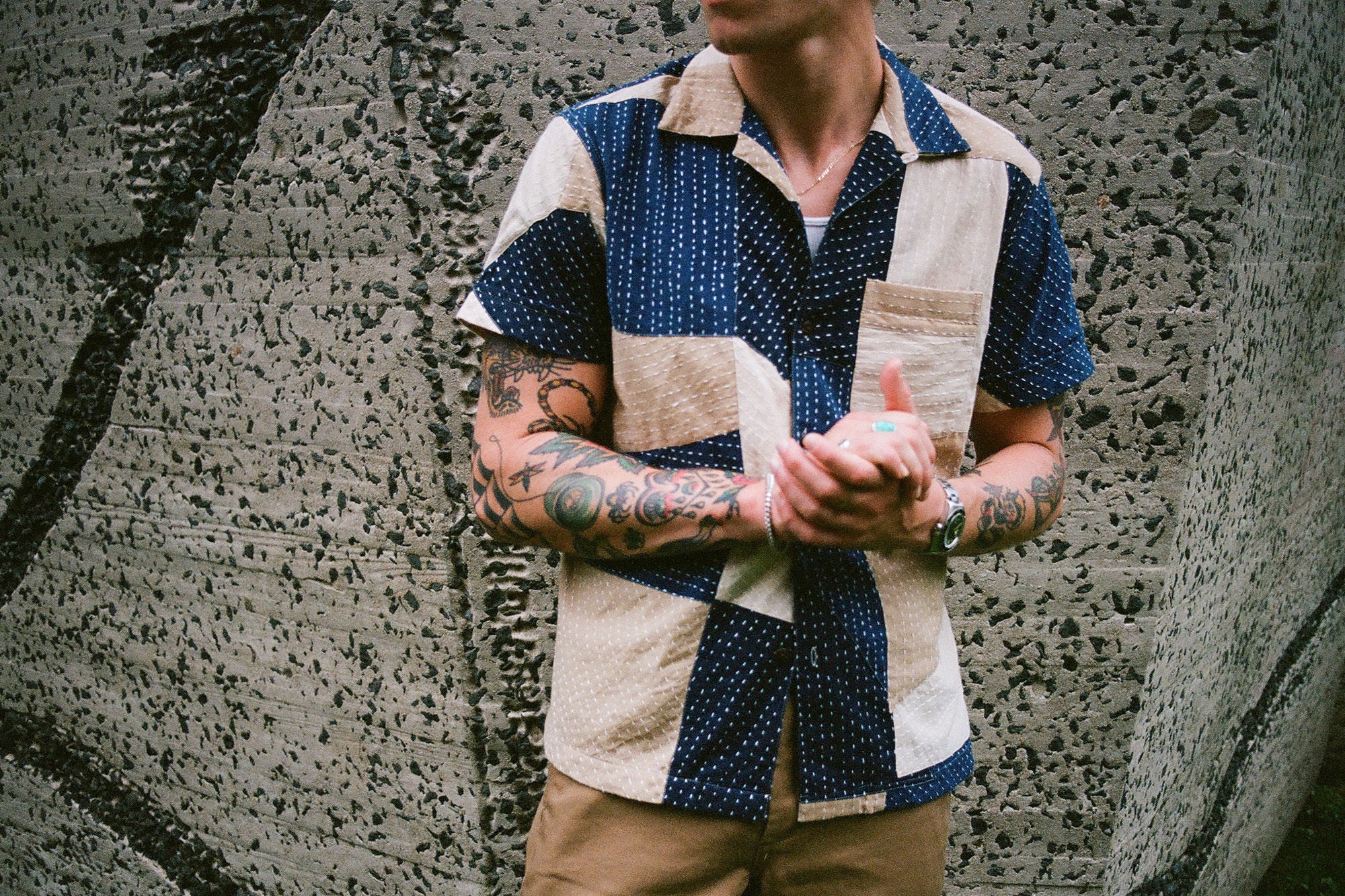 A close up shot of a man's torso who is wearing a patchwork shirt.