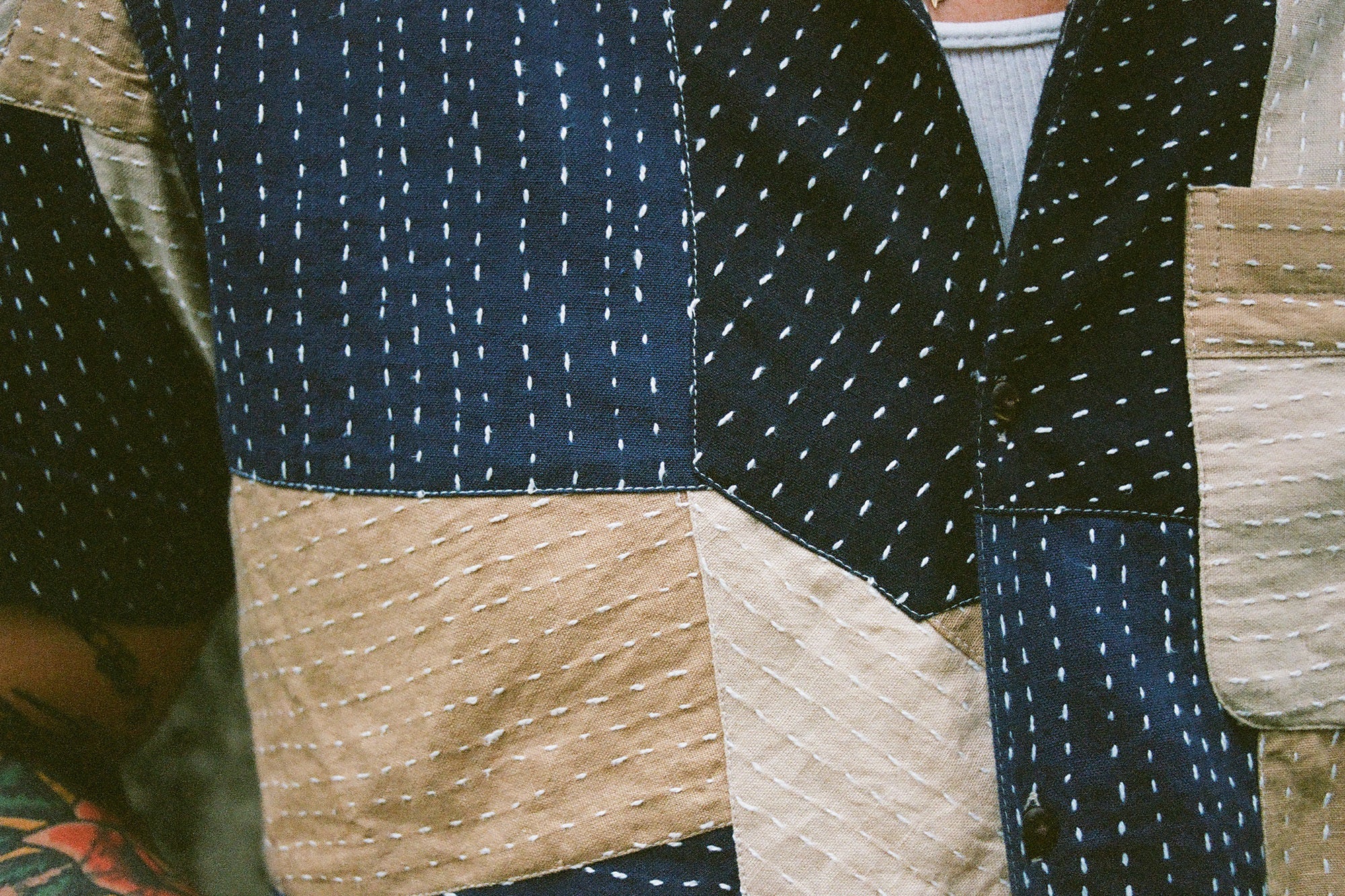 A close up detail of a patchwork shirt showing thick white hand-stitched threads throughout.