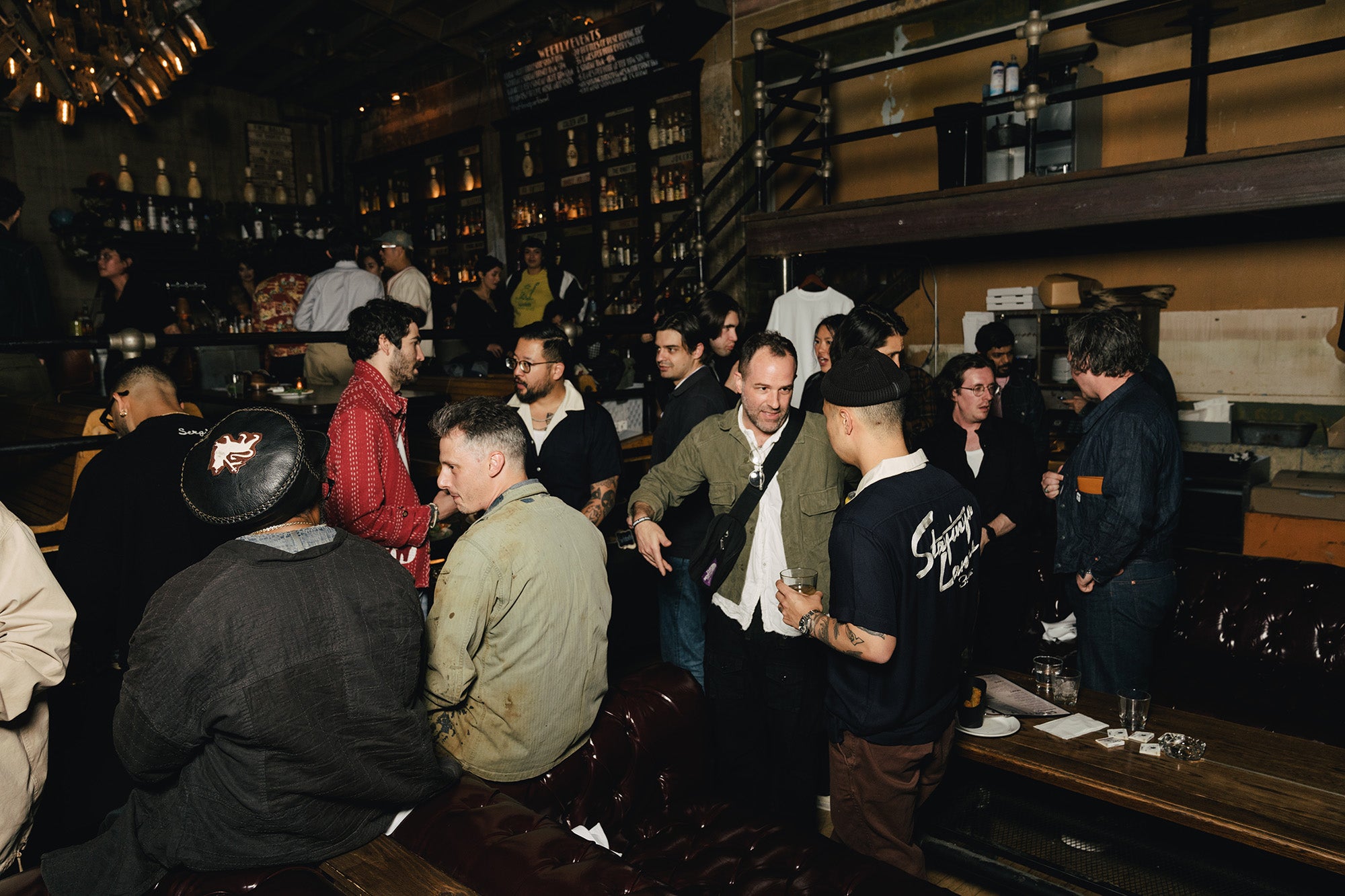 A group of people eating, drinking and chatting in a bowling alley.