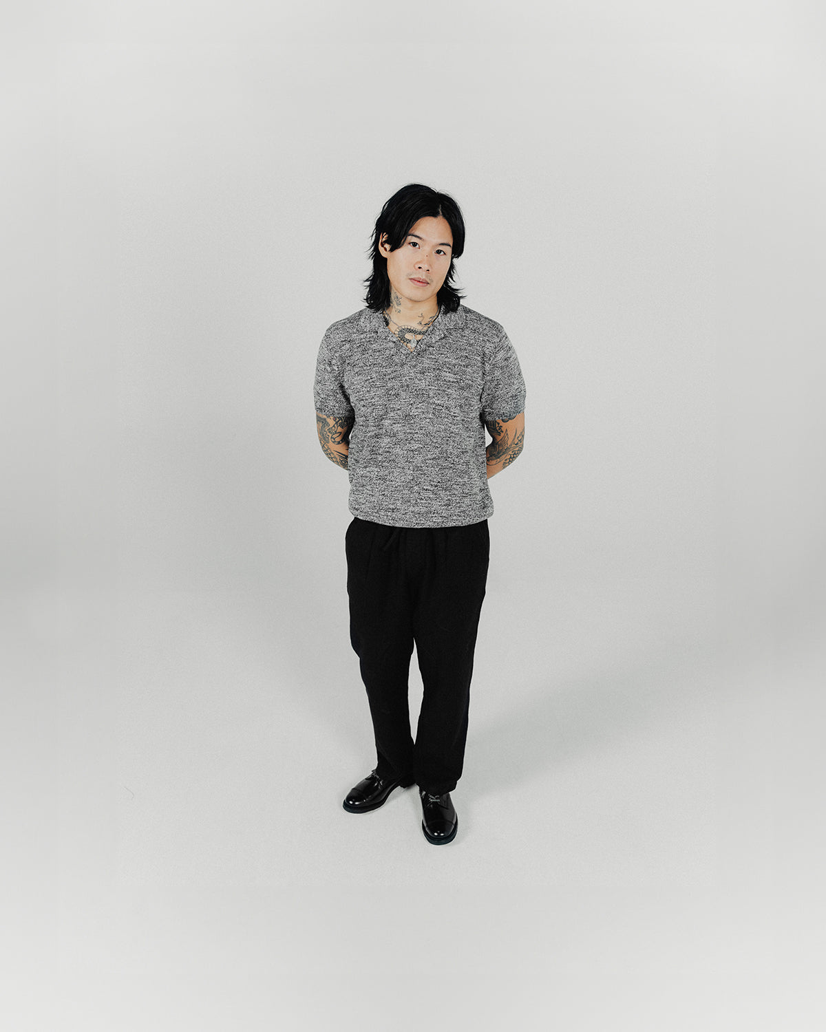 A man poses in a grey knit polo and black pants.