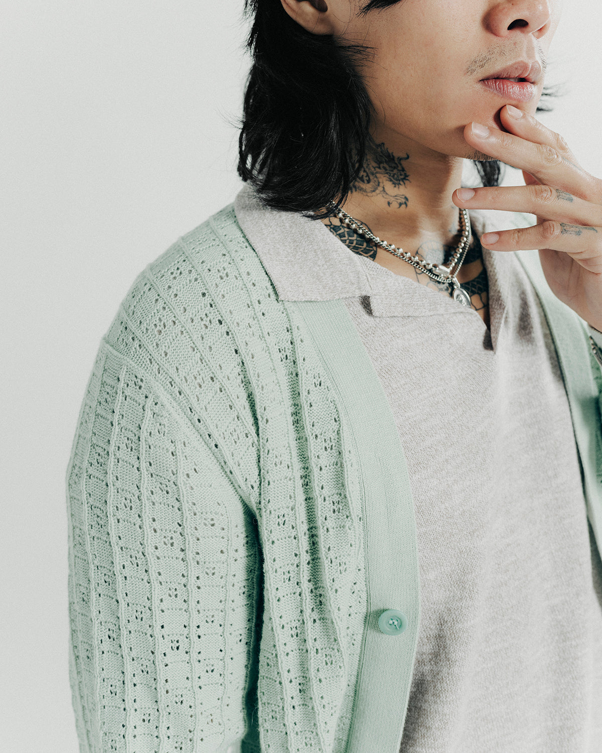 A man poses in a seafoam cardigan layered over a knit polo