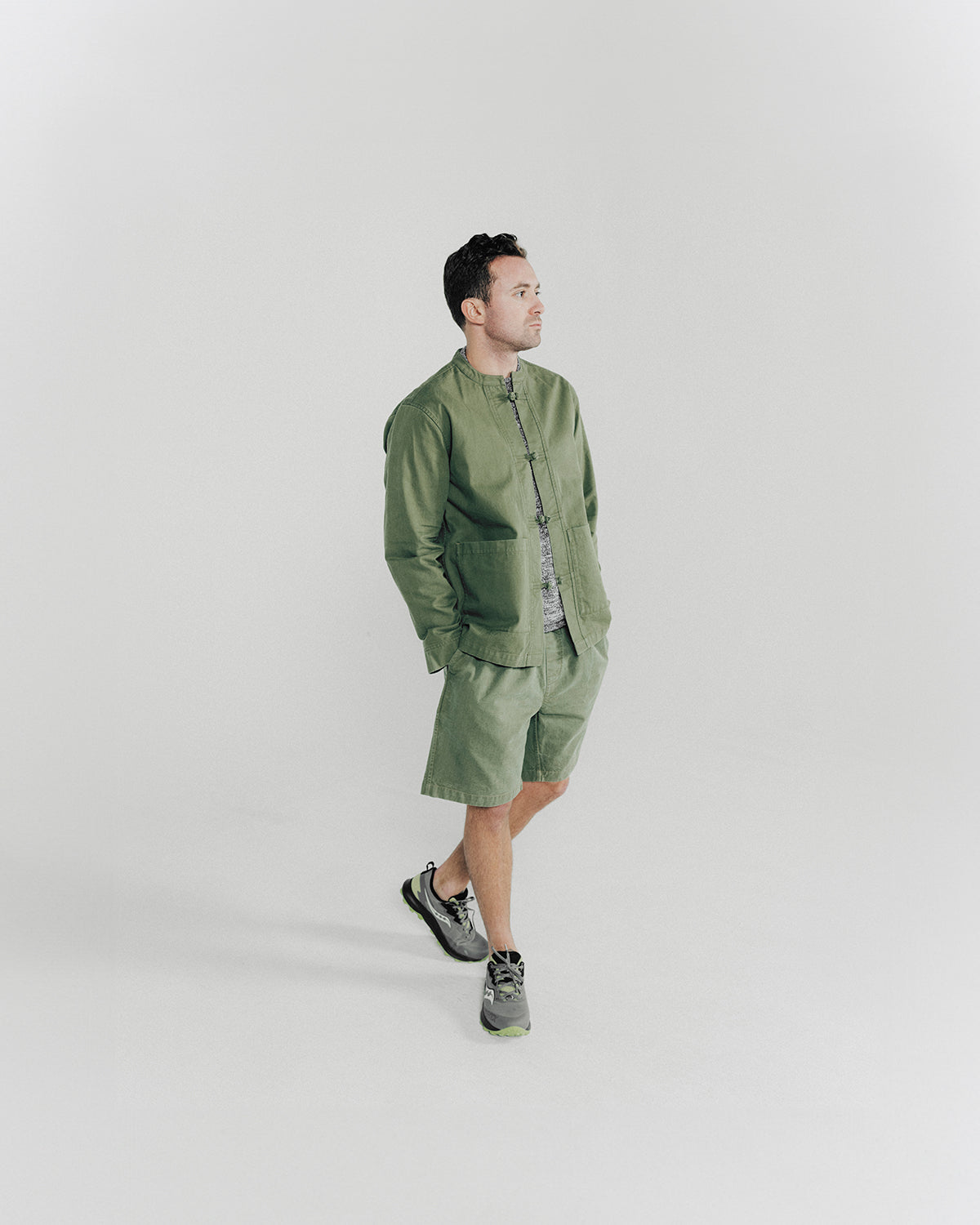 A man poses in an olive jacket and shorts.