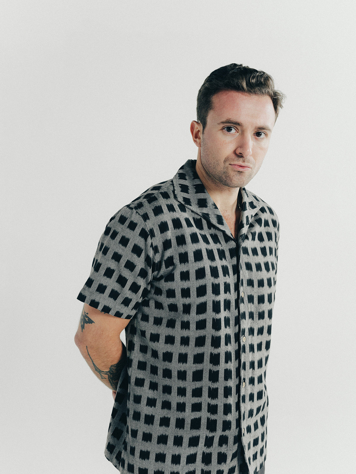 A man poses in a patterned black short sleeve shirt.