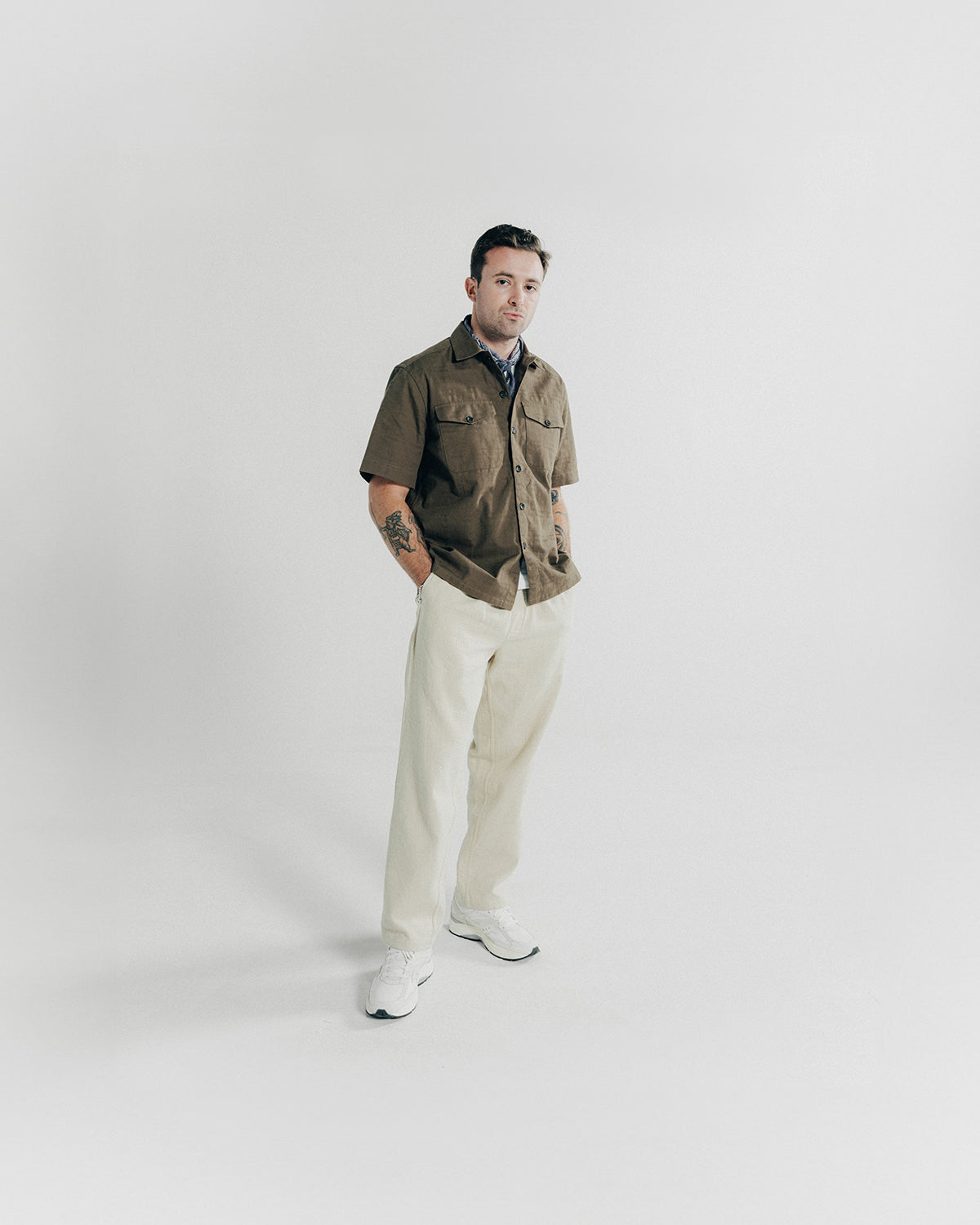 A man poses in a brown shirt and white pants.