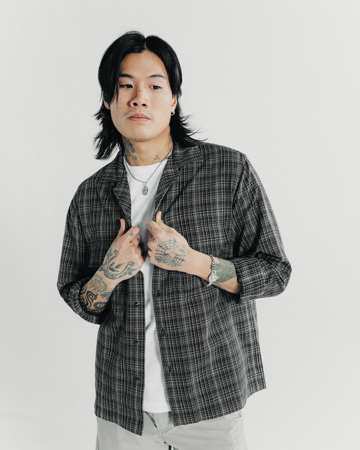 A man poses in a black collared shirt and white tee.