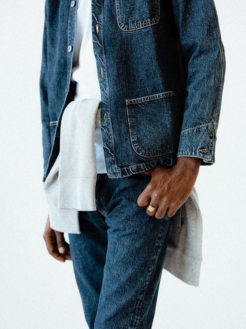 A close up shot of a man wearing a blue denim jacket, jeans, and a sweatshirt tied around his waist.