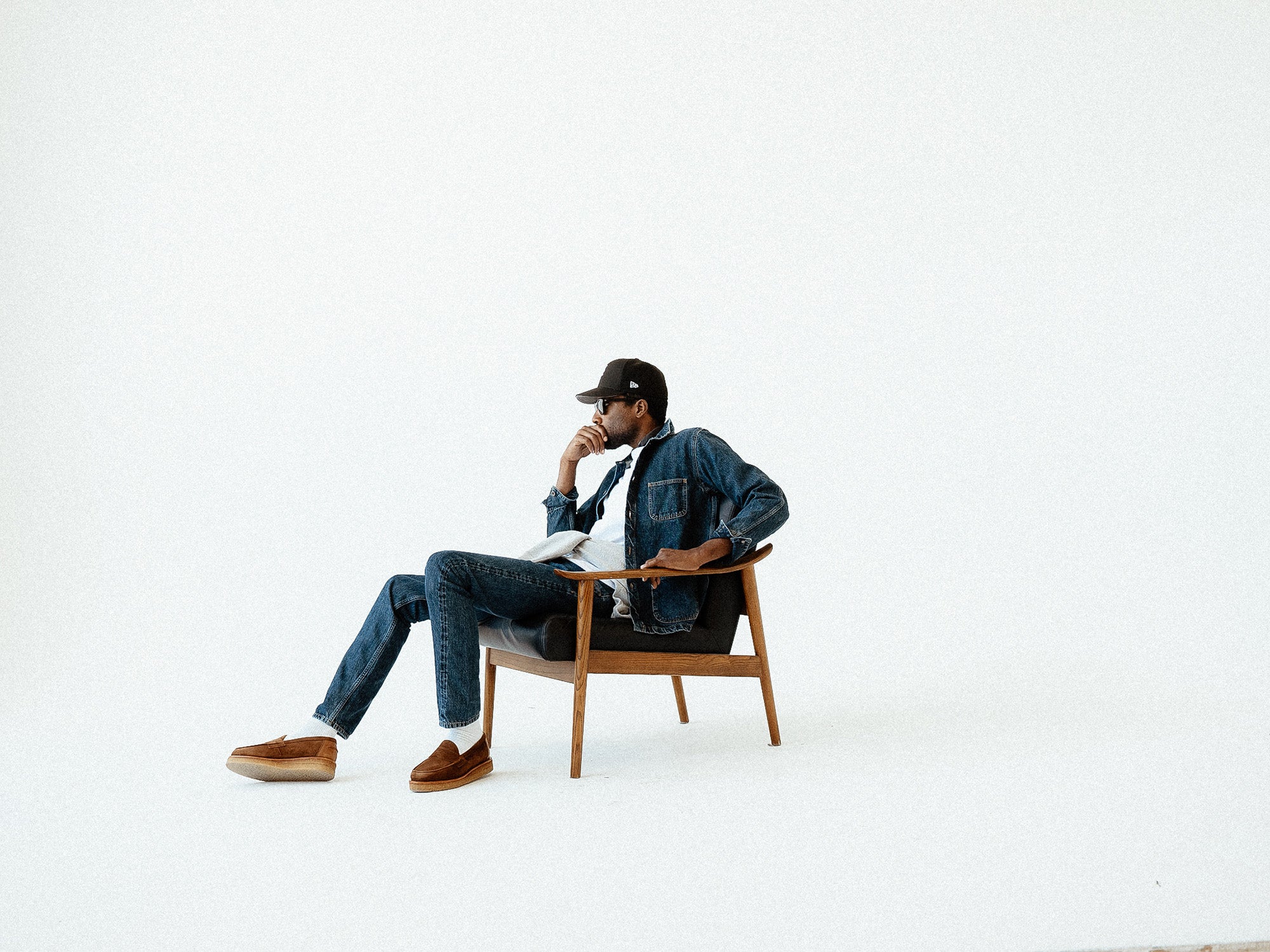 A man in a denim jacket and jeans sits in a black leather chair.