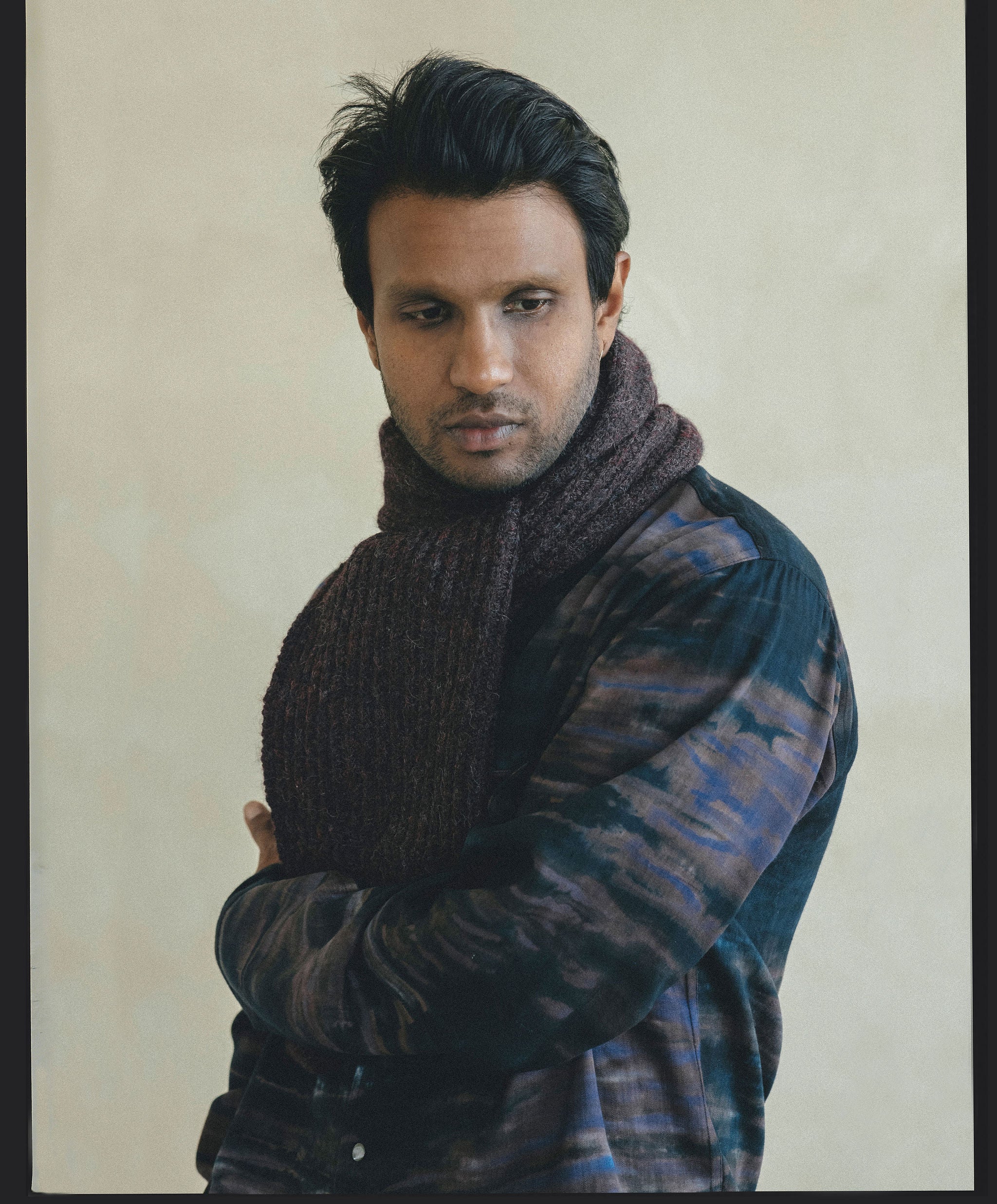 A man in a deep navy patterned shirt and burgundy scarf looks towards the ground.