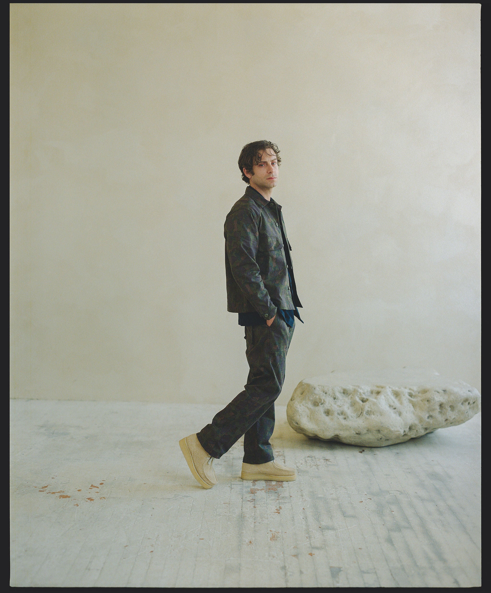 A man in a matching dark camouflage shirt and pants walks across the screen.