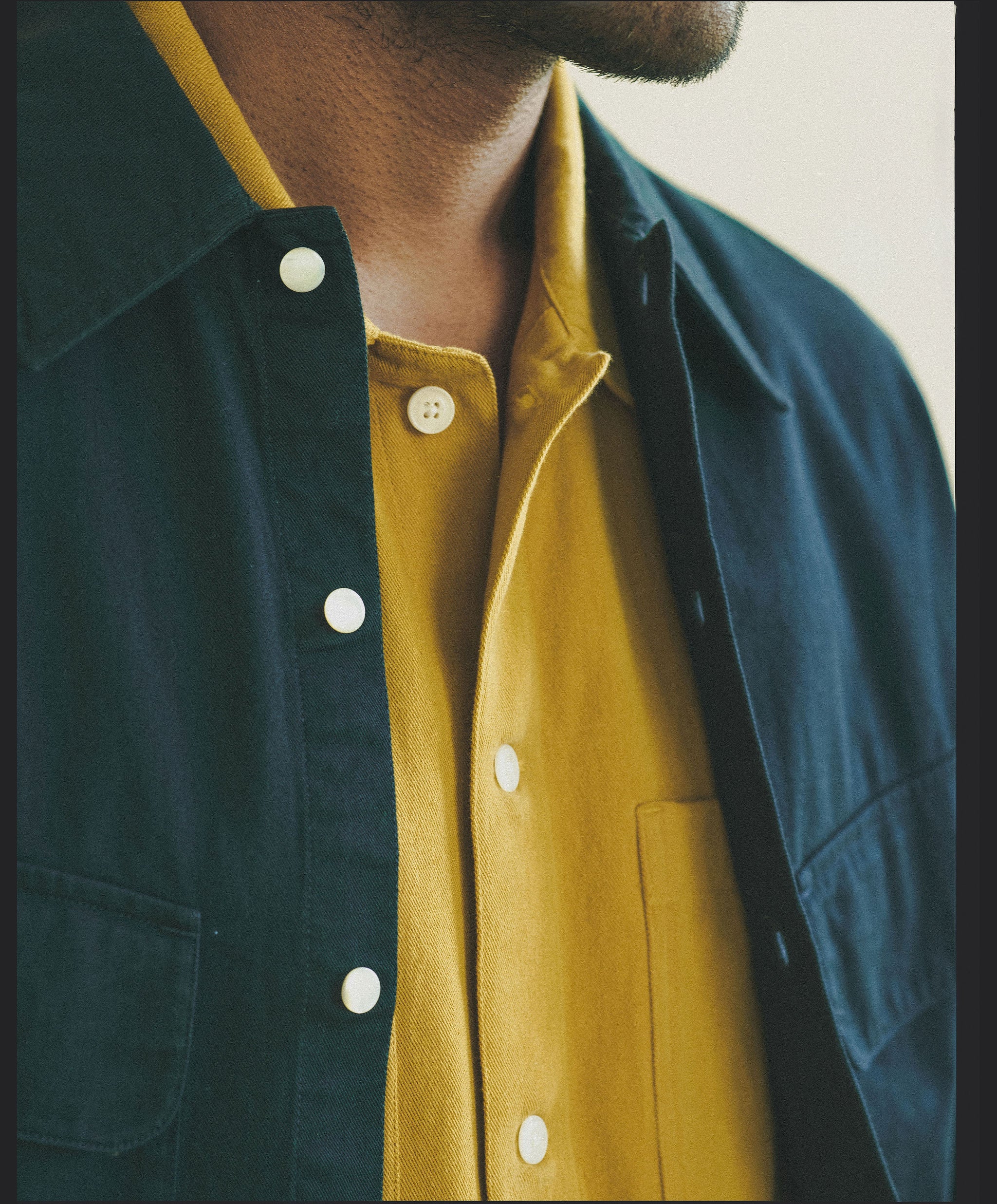 A close up image of a navy overshirt layered over a yellow button down.