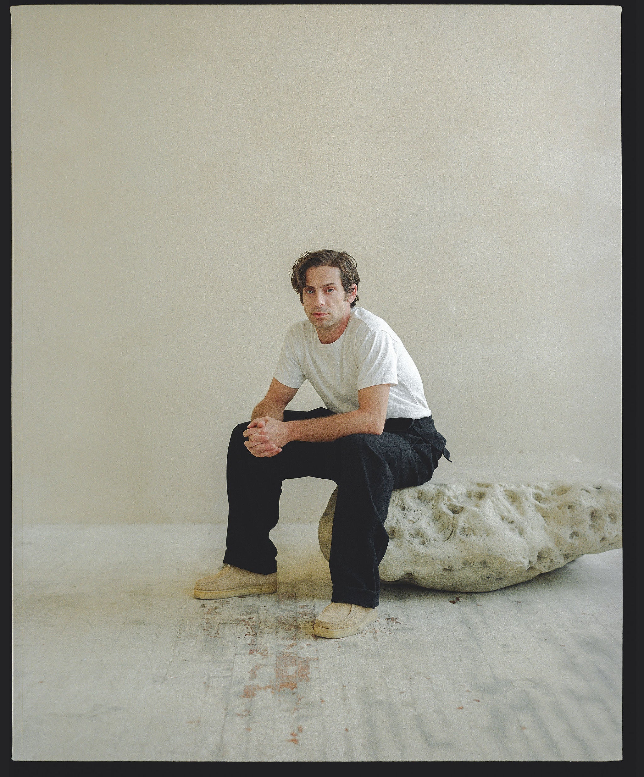 A man in a white tee and black pants sits on a rock.